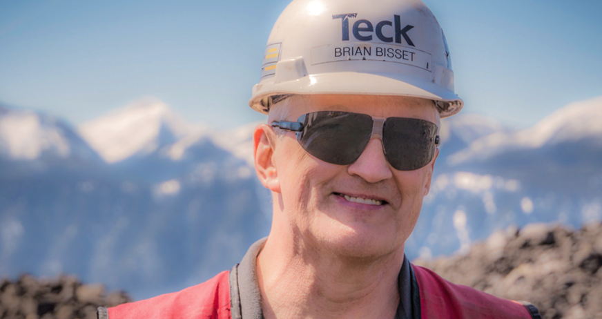 Man in hard hat and sunglasses with mountains in background.