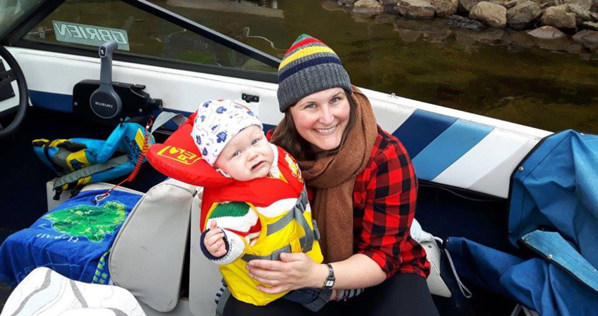 Smiling woman and baby wearing life jacket on a boat.