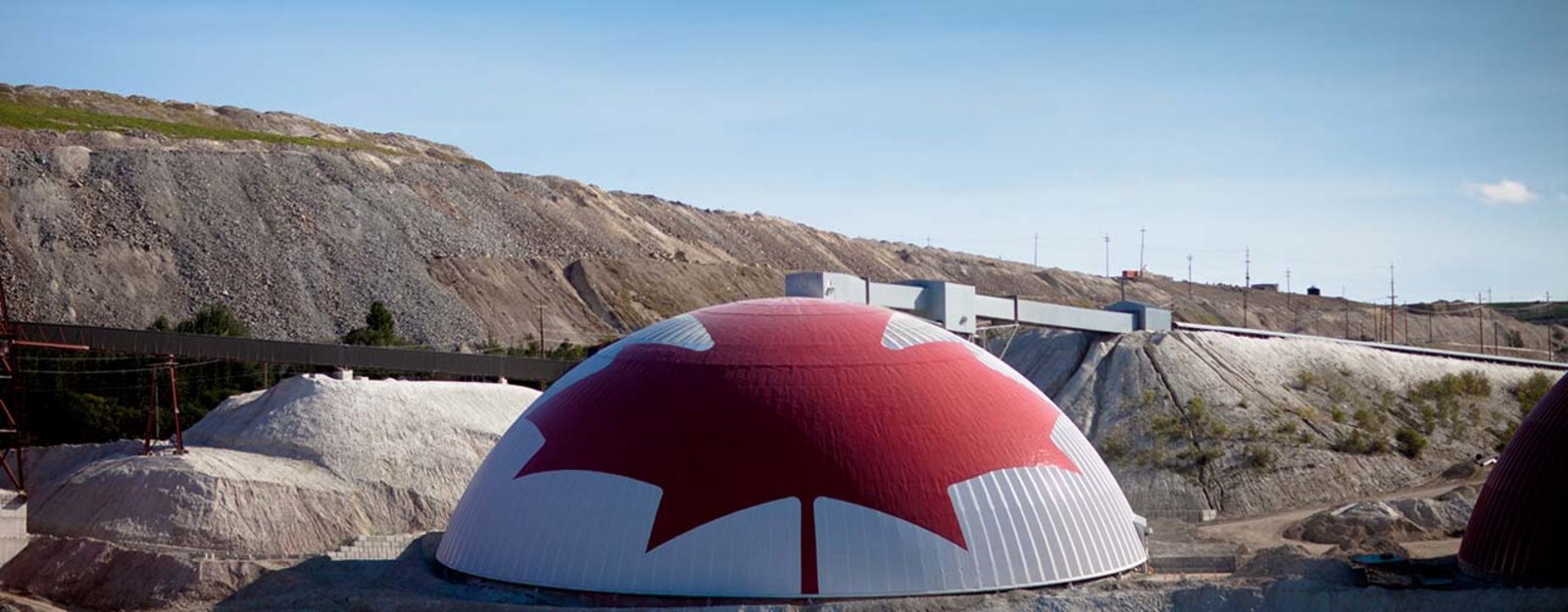 Dome with a large red maple leaf design at a mining site with rocky hills in the background.