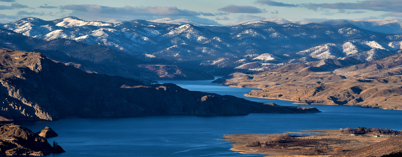 Aerial view of a winding river in a mountainous landscape with snow-covered peaks in the background.