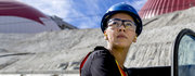 Construction worker in a blue hard hat and safety glasses looks off into distance at a work site.