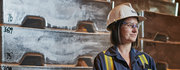 A woman in safety gear and helmet stands in an industrial setting.