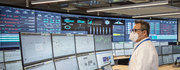 A person in a control room monitors various data and systems on multiple screens.
