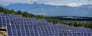 A field of solar panels with mountains in the background under a partly cloudy sky.
