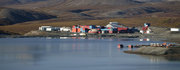 Industrial buildings near a large body of water surrounded by hills, under clear skies.