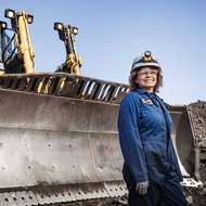 Woman in safety gear standing in front of construction equipment at an industrial site.