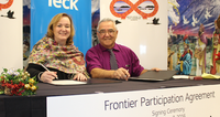 Two people sitting at a table, signing a Frontier Participation Agreement, smiling at the camera.
