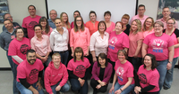 A group photo of 25 people wearing pink shirts with anti-bullying messages, standing and smiling.