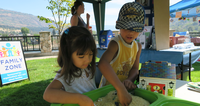 Two children playing with sensory bins at an outdoor family event.