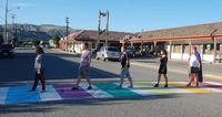Five people crossing a street on a colorful rainbow-painted crosswalk in a quaint town.