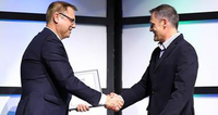 Two men in suits shaking hands, one holding a certificate on a stage.