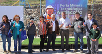 Group of people at a mining technology fair holding small objects in front of a sign and mascot.