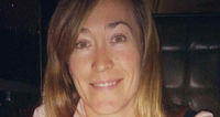 A woman with long hair smiling at the camera, seated indoors.