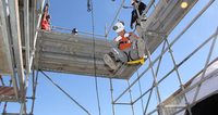 Worker in safety gear performs a rope descent from scaffolding on a clear, sunny day.