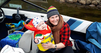 Smiling woman and baby wearing life jacket on a boat.