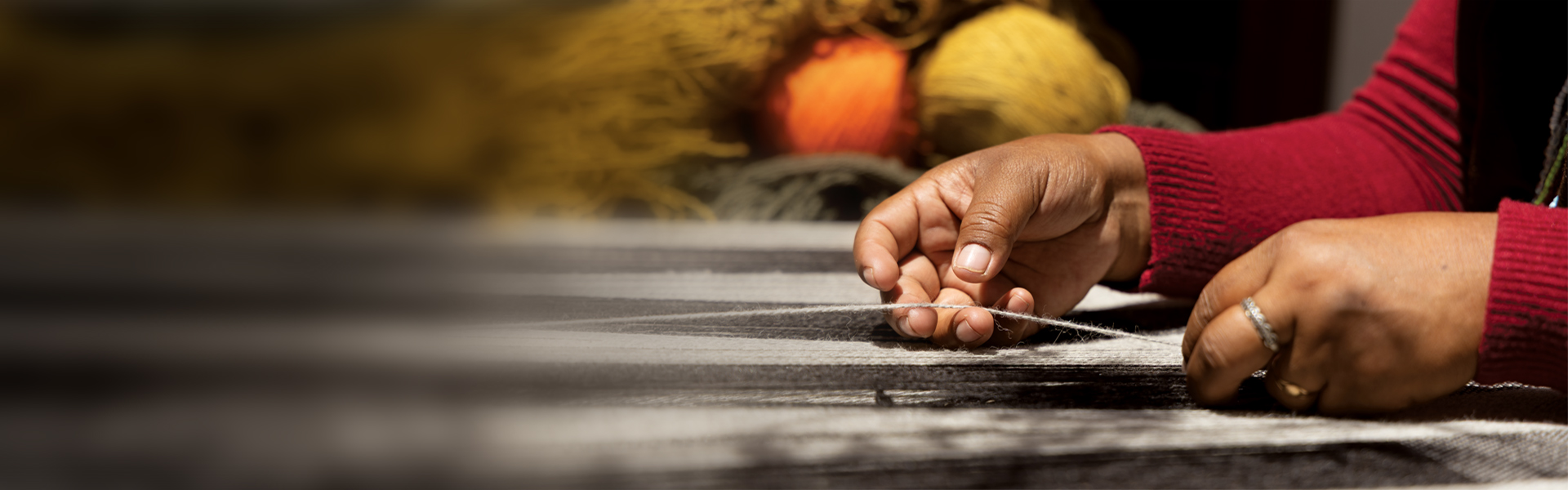 Weaver's hands crafting with threads, colorful yarns in the background.