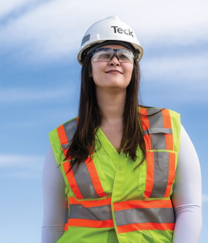 Person in high-visibility vest and hard hat with logo, looking at sky on a clear day.