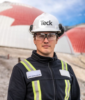 Construction worker in safety gear stands before large red and white domed structure.