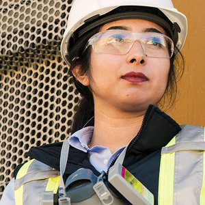 Person in safety gear, including a white helmet and safety glasses, looking off into the distance.