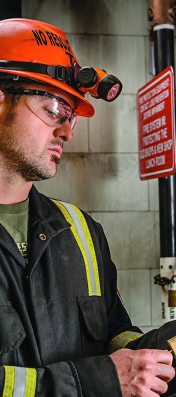 A worker wearing safety gear and helmet with a headlamp in an industrial setting.