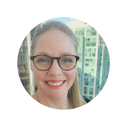 Woman with glasses smiling in front of a cityscape.