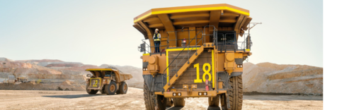 Two large mining trucks with numbered sides on a dirt road at a mining site.