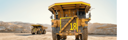 Large mining trucks in a quarry, with a worker standing on the front of truck number 18.