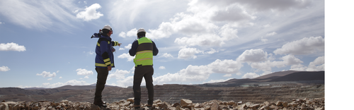 Two engineers inspect a mining site under a cloudy sky.