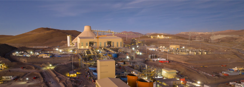 Panoramic view of a mining facility at dusk with surrounding hills and illuminated buildings.