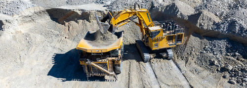 Excavator loading dirt into a large dump truck at a mining site.