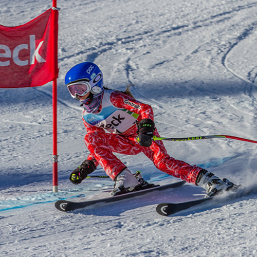 Skier in red suit with a blue helmet navigating a slalom course on a snowy slope.