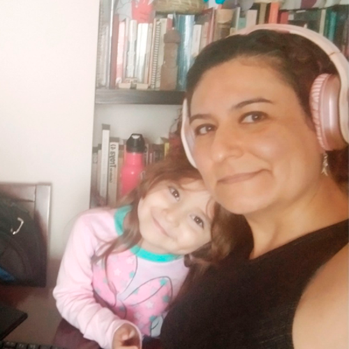 A woman with headphones and a child smile near a bookshelf.