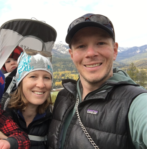 A couple with a baby in a carrier, enjoying a hike with mountains in the background.