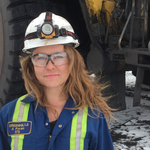 Person wearing a hard hat and safety goggles, standing in front of industrial equipment.