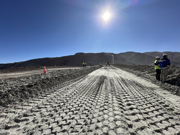 Construction site with workers, dirt road, and bright sunny sky in mountainous area.