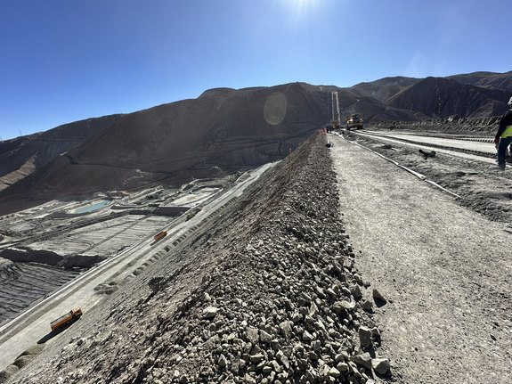 Gravel road at a mining site on a sunny day, with mountains in the background.