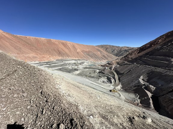Open-pit mining site in arid mountains under clear blue sky.