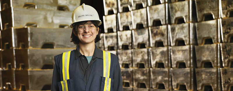 Person wearing safety gear and a hard hat, standing in front of metal blocks in an industrial setting.