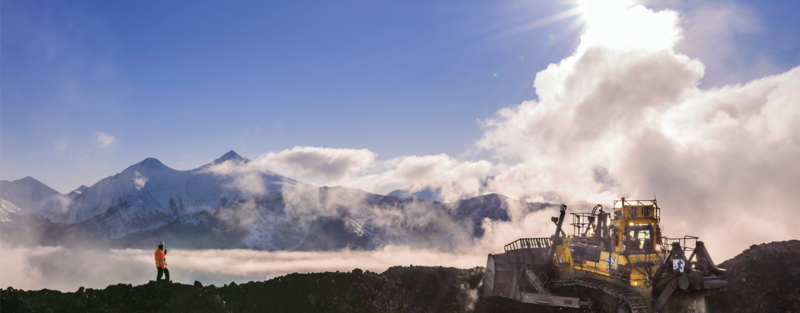 A person and heavy machinery in a mountainous, mist-covered area under a bright sky.
