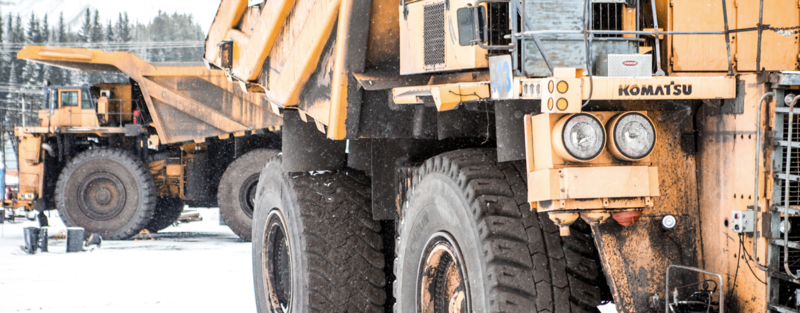 Two large Komatsu dump trucks parked in a snowy industrial yard.