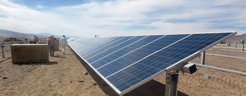 Workers near large solar panels in a desert environment under a partly cloudy sky.