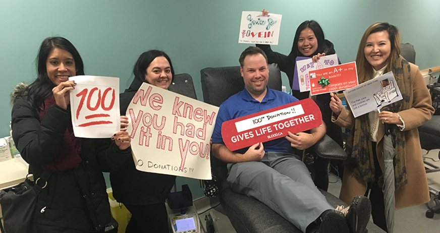 Group at a blood donation center holding supportive signs, donating blood.