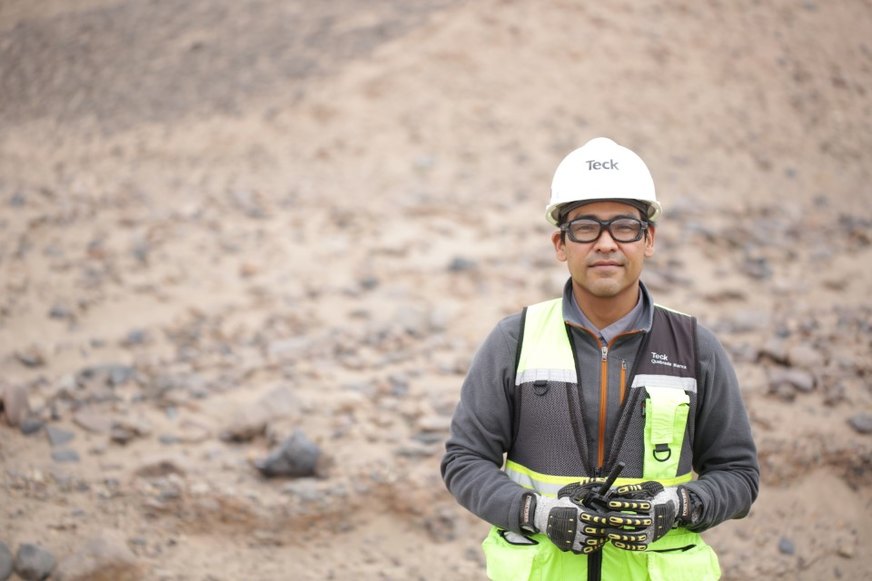A person wearing safety gear, including a hard hat and vest, standing in a rocky outdoor environment.