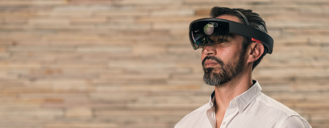Man wearing augmented reality headset, standing against a wooden background.