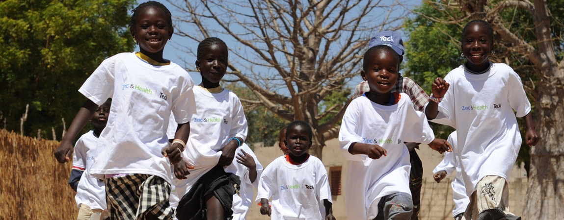Global Citizenship Group of children in white t-shirts running outdoors on a sunny day.