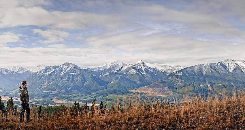 Person standing on hilltop with scenic view of mountains under a partly cloudy sky.