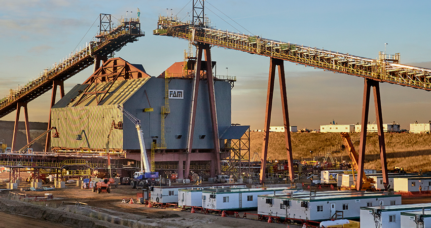 Industrial facility with conveyor belts and large structures, surrounded by portable buildings.