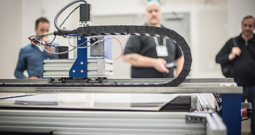 A CNC machine in operation with three people observing in the background.