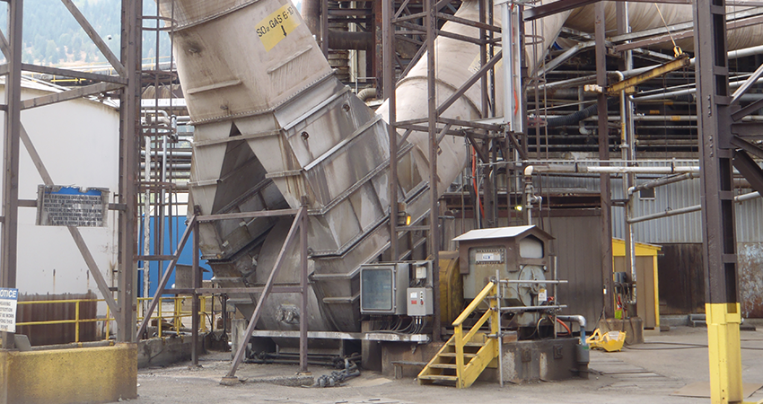 Industrial equipment with metal structures, pipes, and stairs in a concrete and metal facility.