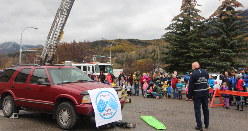 A roadside emergency demonstration with a fire truck, red SUV, and onlookers in a mountainous area.